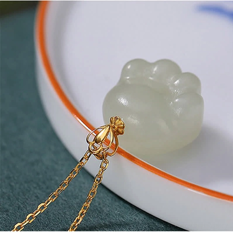 Hetian white jade cat paw pendant and detachable gold chain connector on white plate with orange rim showing smooth jade texture