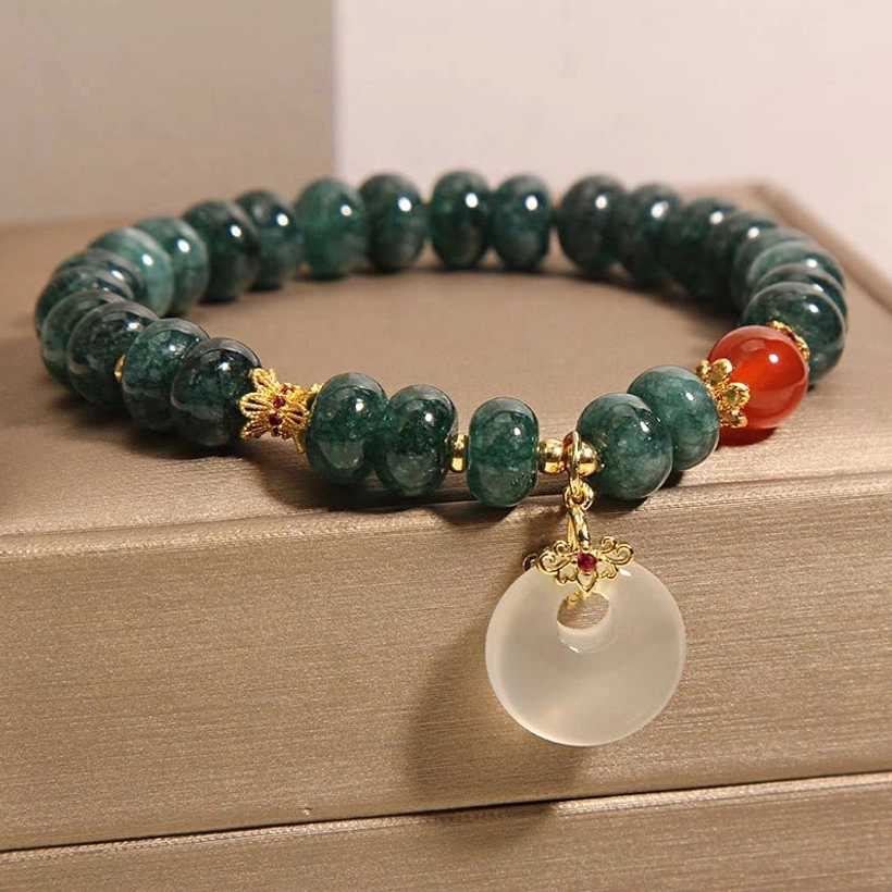 Three-quarter side view of jade charm bracelet with white peace buckle pendant in display box, showing craftsmanship details