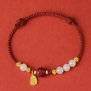 Red string jade bracelet with cinnabar bead and gold accents top-down circular view