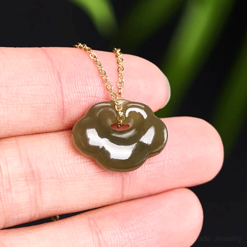 Hand-held jade cloud lock pendant showing deep forest green Hetian jade and refined carved detail in natural light