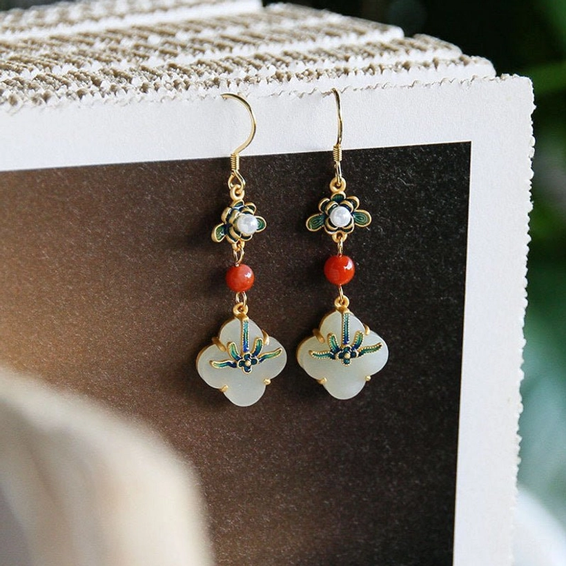 Four leaf clover jade earrings with enamel flower design and red bead on textured background