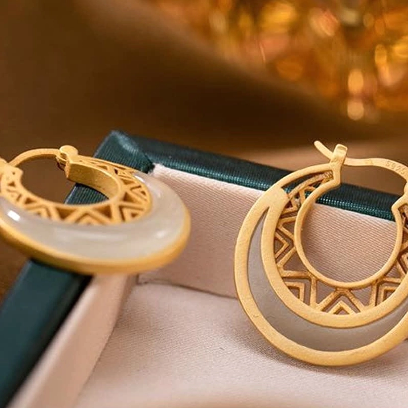 Side close-up view of jade crescent moon earrings on luxury jewelry box, showing layered structure, light beige jade, and matte gold frame