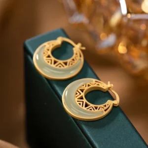 Close-up side view of jade crescent moon earrings on luxury green jewelry box with golden accents, displaying light green jade and matte gold finish
