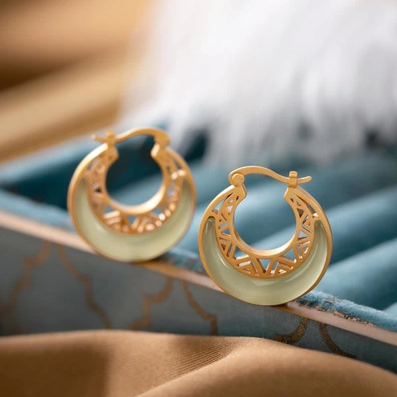 Pair of jade crescent moon drop earrings displayed on blue velvet jewelry tray, high-angle front view showing geometric hollow carvings