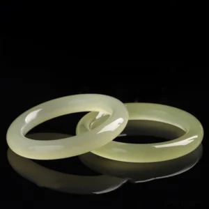 Two interlocked Afghanistan jade bangles close-up on black studio background, highlighting glossy polished finish and light pale yellow-green tone