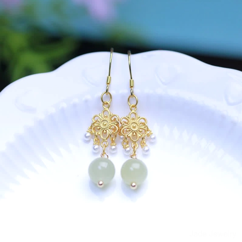 Overhead flat lay of pair of hetian jade flower dangle earrings with light green jade beads and delicate gold flower design on plate
