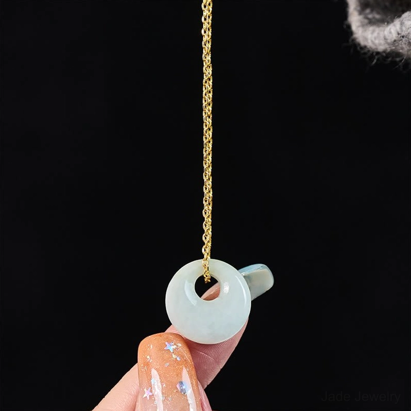 Single natural jade donut pendant close-up on black background held by decorated fingernail