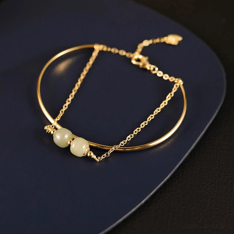 Top down close up of double layer jade bangle bracelet with two light green beads showing layered design on dark tray