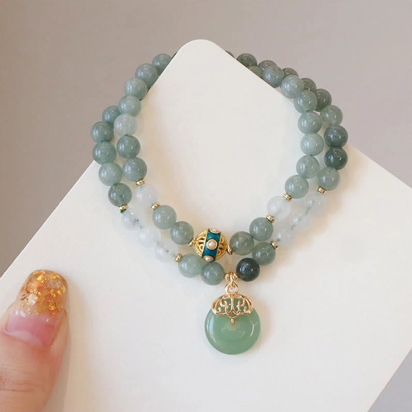 Double strand jade bracelet with peace buckle pendant featuring mixed jade beads, gold enamel charm, and jade peace buckle on wooden display