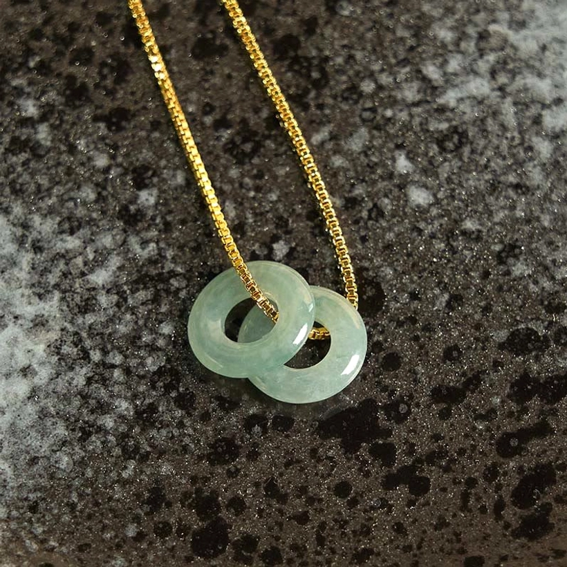 Double polished jade peace buckle pendant with gold box chain, overhead detail view on stone surface