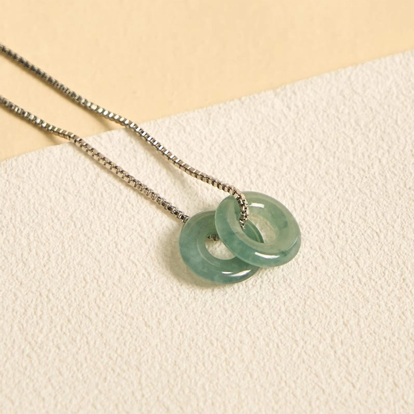 Double jade peace buckle pendant necklace with chain, artistic flat lay composition on decorative background