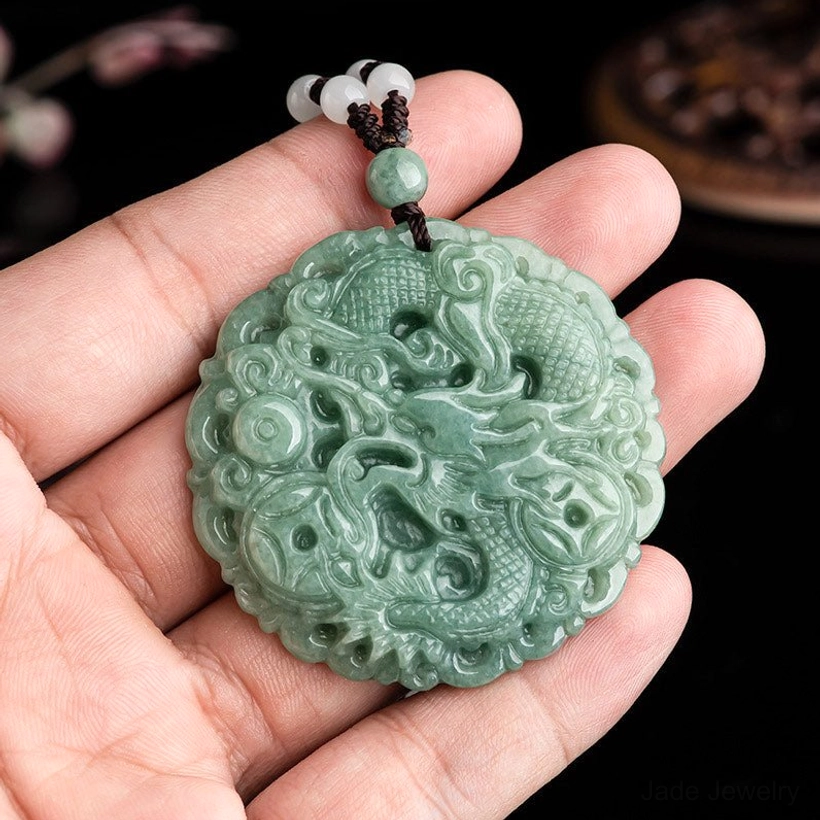Close-up of jade dragon pendant held in hand showing actual size and carving quality with brown beaded cord