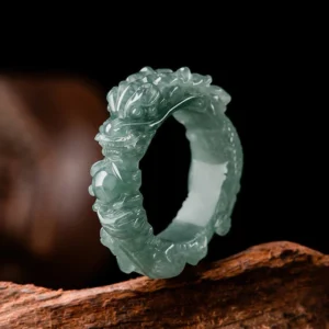 Natural jade dragon ring with intricate hand-carved dragon design, displayed on weathered wood surface showing deep teal jade green color and detailed dragon carving