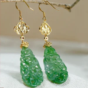 Close-up overhead view of carved Hetian jade drop earrings featuring filigree gold hardware, red gem accents, and hollow green jade pendants