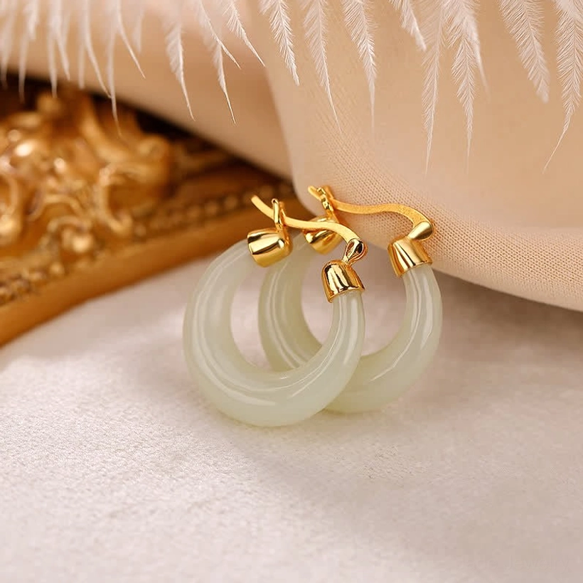 Pale natural jade hoop drop earrings flat lay on satin with vintage golden frame and feather decor, showing smooth polished jade finish and gold hardware