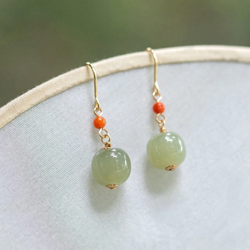 Traditional Chinese style jade drop earrings with red agate accents photographed at eye level against antique silk fan backdrop