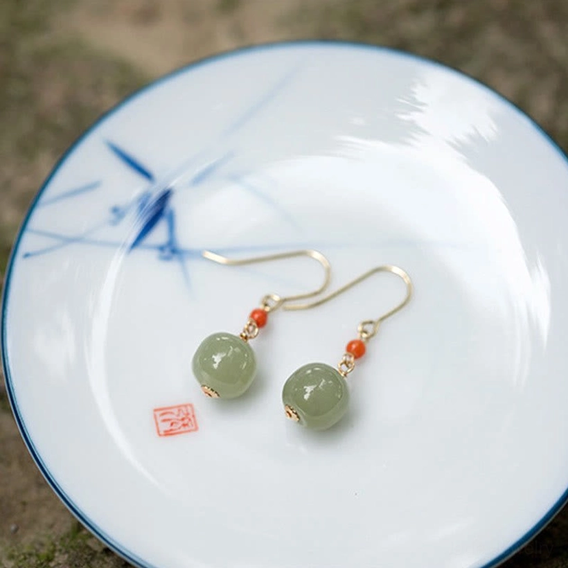 Symmetrical pair of jade drop earrings with red agate beads on blue-patterned porcelain plate with red seal accent
