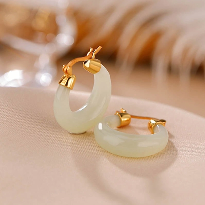 Two natural jade drop earrings photographed from oblique angle on satin with warm-toned golden decor background, highlighting smooth curved jade design