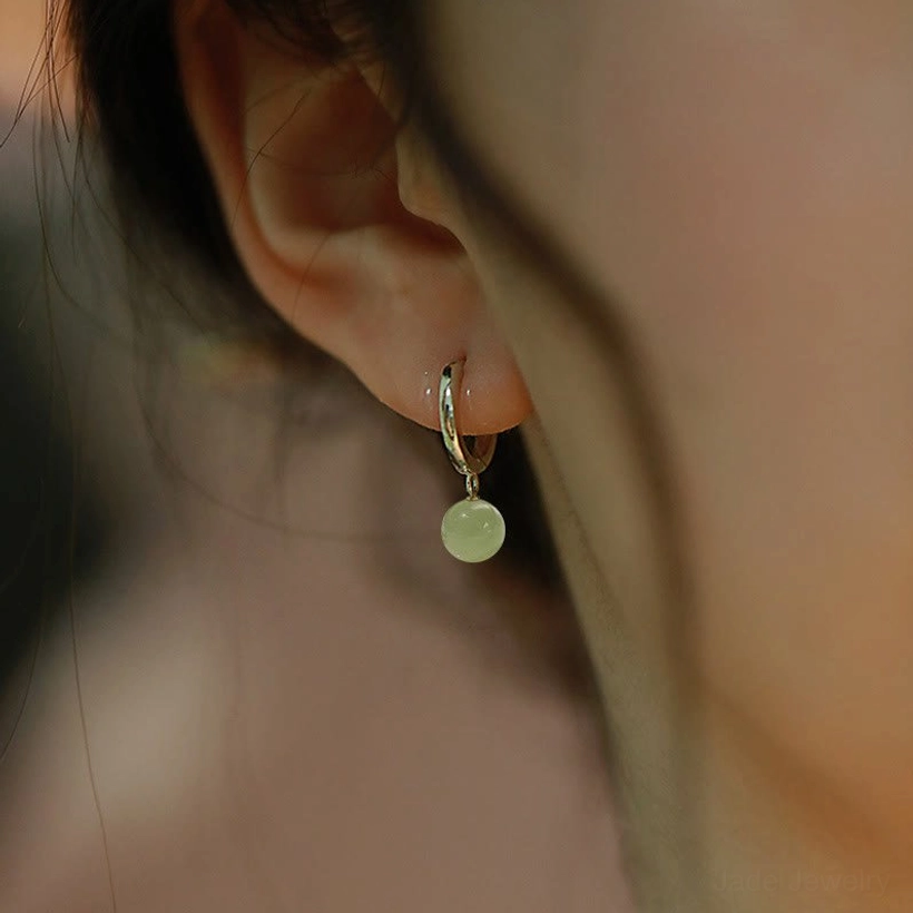 Single jade bead hoop earring worn on earlobe, light green jade charm on sterling silver hoop close-up