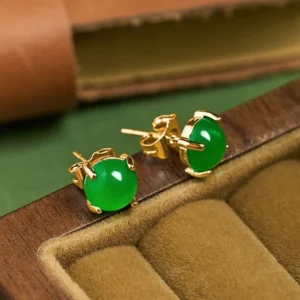 Jade stud earrings displayed in velvet-lined wooden jewelry box showing gold hardware and emerald green stone