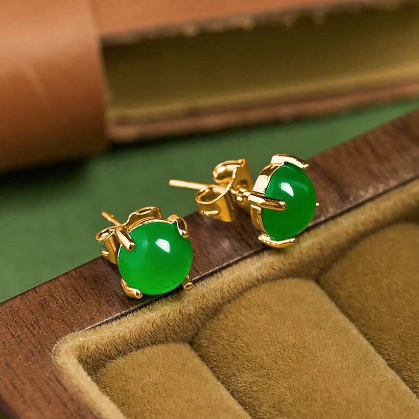 Jade stud earrings displayed in velvet-lined wooden jewelry box showing gold hardware and emerald green stone
