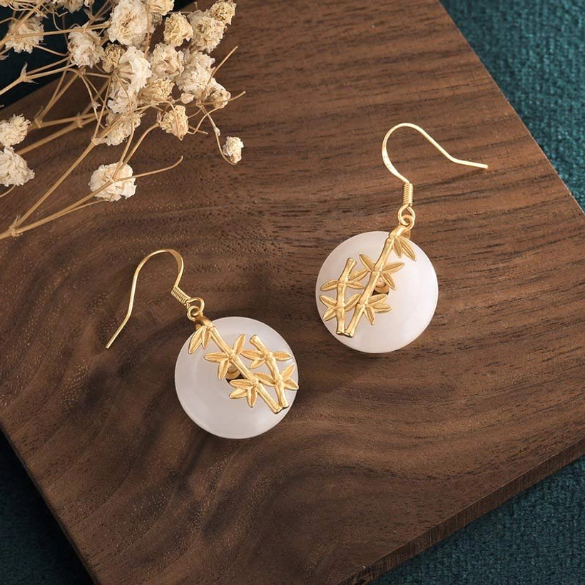 Handcrafted jade drop earrings detail view - close-up of jade stone and bamboo charm on wooden background