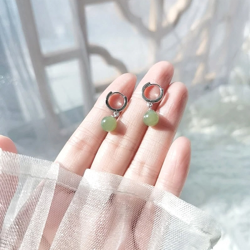 Jade bead hoop earrings held on fingertips in soft window light, sheer fabric backdrop, close-up jewelry view