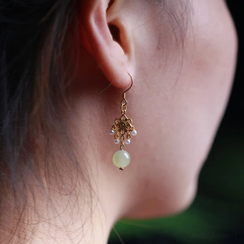 Close-up of hetian jade dangle earrings worn on earlobe showing comfortable fit and elegant drape of light green jade pendant