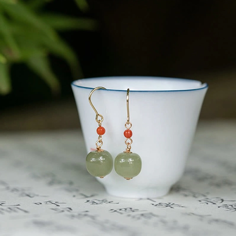 Chinese jade drop earrings displayed with white tea cup and traditional calligraphy paper styling