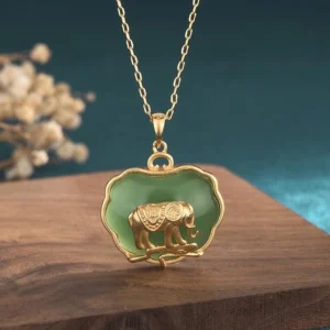 Natural jade elephant pendant necklace with gold-plated copper scalloped frame and polished green jade inlay, displayed on wooden table with dried floral decoration