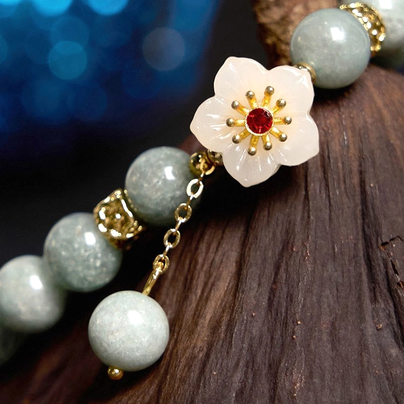 Close-up side view of jade flower bracelet showing gold metal connectors, creamy white floral charm, and dangling smooth jade bead