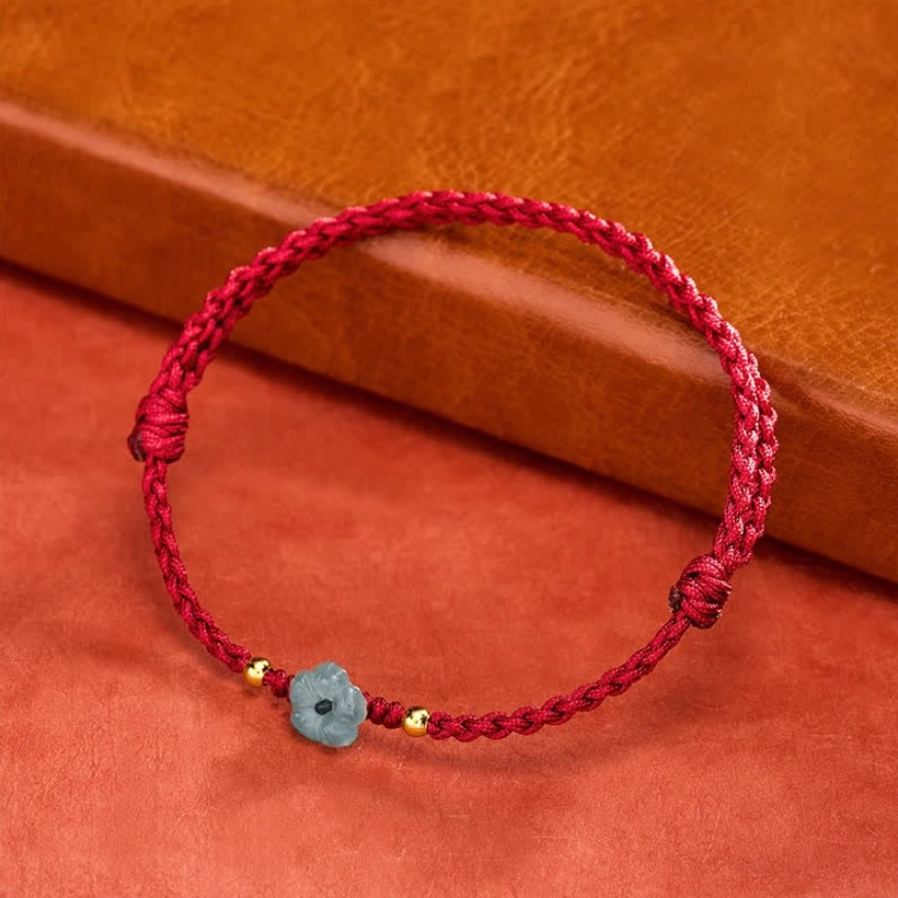 Red string jade flower bracelet three-quarter angle displaying braided cord and blue jade flower charm on wooden background