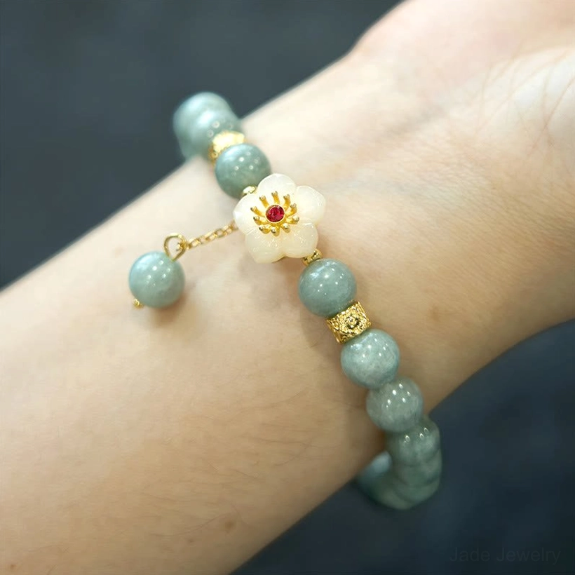 Jade flower bracelet worn on left forearm with gold accent beads and dangling jade charm against dark background