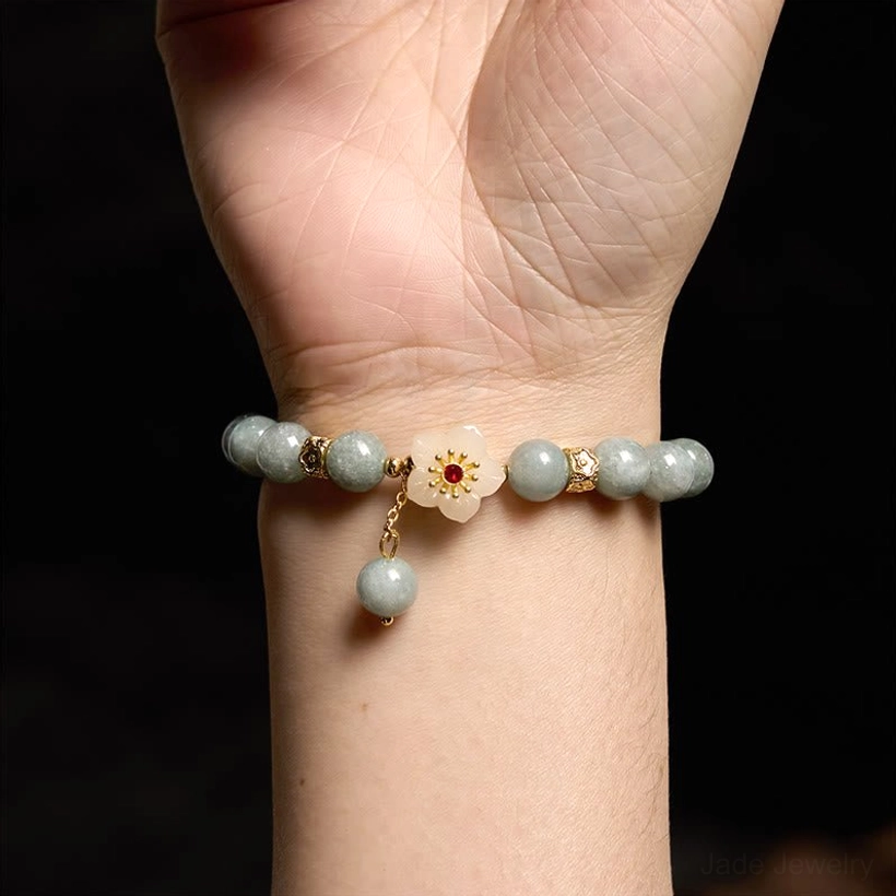 Jade flower bracelet worn on right wrist, overhead view showing compact floral pendant with dangling jade bead
