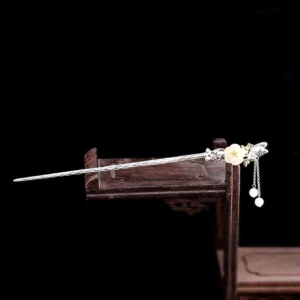 White jade flower hairpin with silver butterfly ornament resting on traditional wooden Chinese stand, side profile view