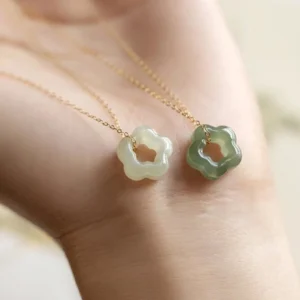Delicate jade flower pendant necklace worn on wrist close-up showing light and dark green pendants fine gold chain