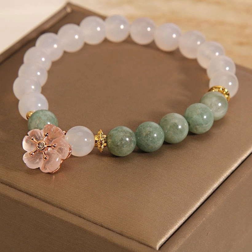 Prominent close-up of jade flower charm bracelet showing pink flower pendant and mixed stone beads