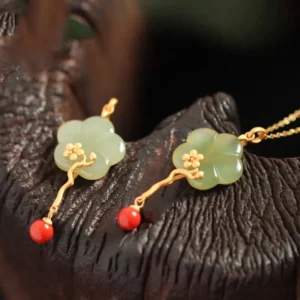Two matching carved jade flower pendants with red agate dangling beads on dark wood surface, displaying handcrafted artistry and design details