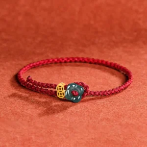 Jade flower red string bracelet with copper coin charm, three-quarter flat lay view showcasing braided red cord, gold copper coin, and dark green jade flower ornament