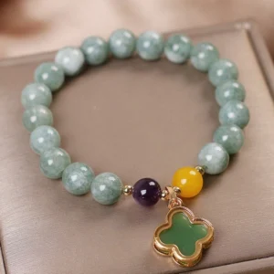 Flat lay overhead view of jade clover charm bracelet resting in satin jewelry tray, showing authentic green jade beads, decorative spacer beads, and delicate gold four-leaf clover pendant