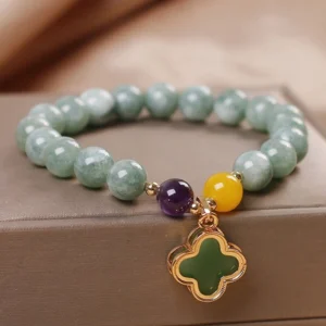 Green jade four-leaf clover luck bracelet displayed on elegant satin jewelry box, featuring premium mottled jade beads with purple and yellow accent stones and gold-plated clover charm