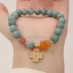 Green jade four leaf clover bracelet worn on wrist showing matte jade beads with gold lucky charm pendant