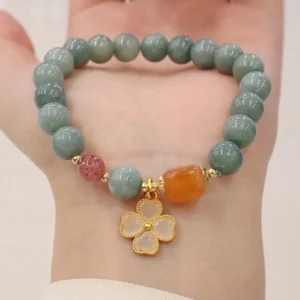 Green jade four leaf clover bracelet worn on wrist showing matte jade beads with gold lucky charm pendant