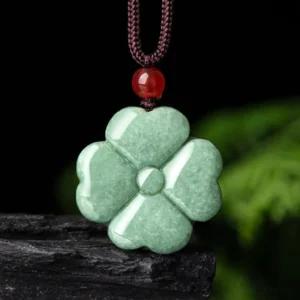 Natural green jade four-leaf clover pendant necklace with red bead accent and brown rope, shown flat against dark stone and green foliage background
