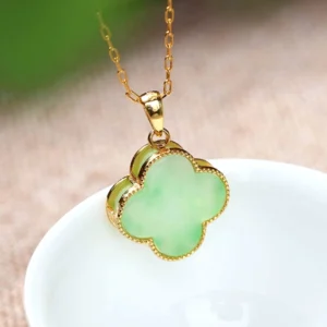 Side close-up view of handmade green jade four-leaf charm pendant with 24K gold-plated metal bezel and delicate gold-tone chain on ceramic background