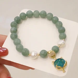 Green jade fox charm bracelet with temperature-changing stone, featuring gold-toned fox pendant and white pearls, displayed on product card