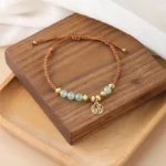 Jade Fu Character blessing bracelet with light green polished beads and gold-toned fu pendant on wooden background
