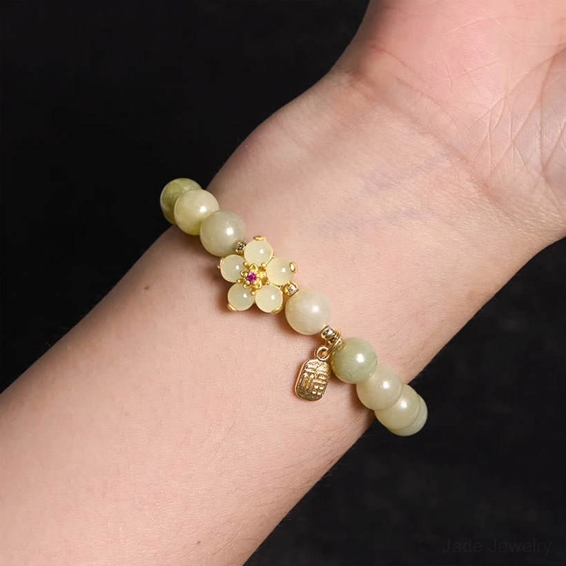 Green jade Fu character bracelet worn on wrist - side close-up view showing light green jade beads with gold flower ornament and dangle Fu pendant