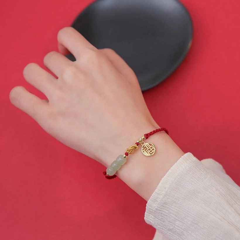 Worn red rope jade Fu bracelet on wrist with white long sleeve shirt - close-up styling view of braided cord and charm