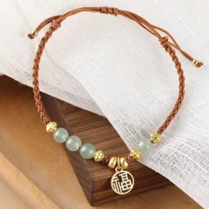 Adjustable jade bracelet with fu character charm, twisted brown rope and gold spacer beads, wooden backdrop